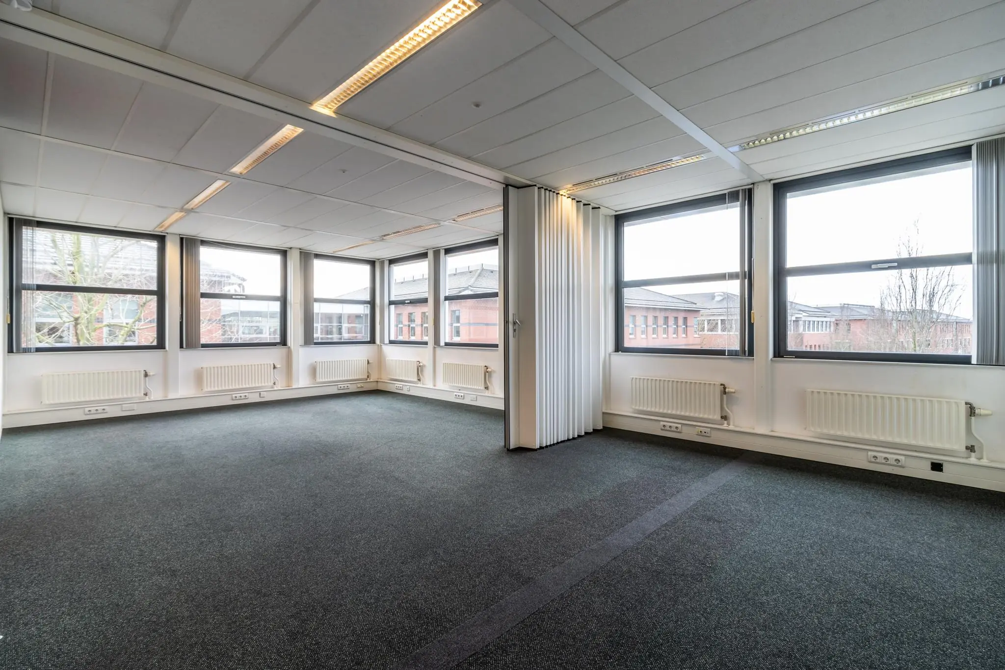 Lichte, lege kantoorruimte aan de Lange Dreef met grote ramen en uitzicht op omliggende gebouwen.